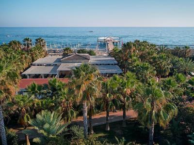 Blick auf Küstenanlage mit Palmen und Gebäuden am Meer unter blauem Himmel.