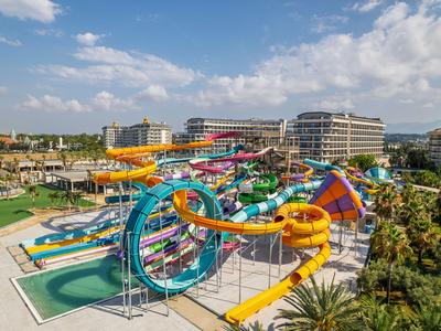 Bunte Wasserrutschen und Pools in einem Wasserpark neben Hotelgebäuden unter blauem Himmel.