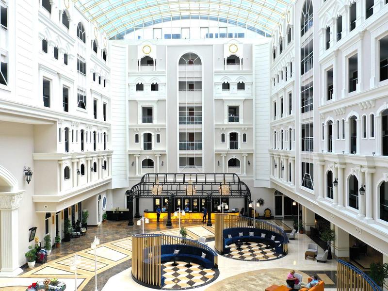 Heller, großer Innenhof mit weißer Fassade, Glasdach und Sitzbereichen auf Marmorfußboden.