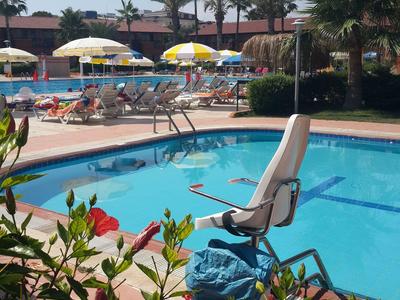 Ein Hotelpool mit Liegestühlen, Sonnenschirmen und Palmen an einem sonnigen Tag.