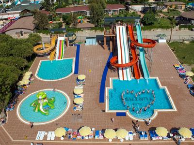Wasserpark mit mehreren Wasserrutschen und Pools, umgeben von Liegestühlen und Sonnenschirmen.