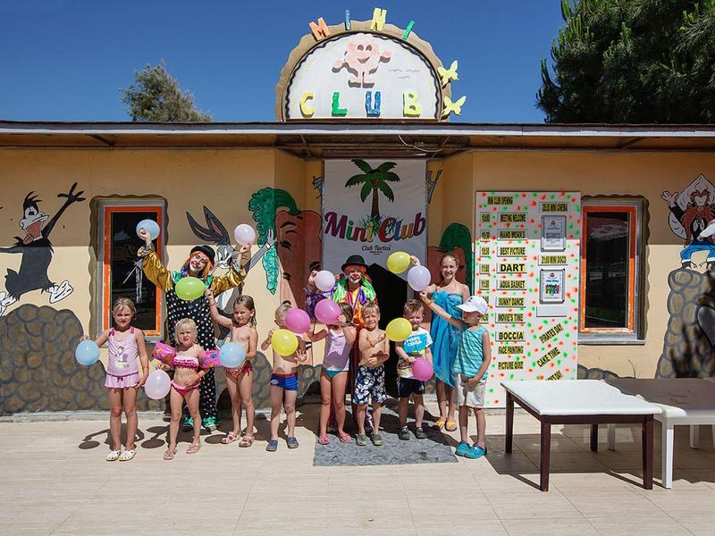 Kinder stehen vor einer bunt bemalten Wand mit Ballons und Sommerdekoration bei Sonnenschein.