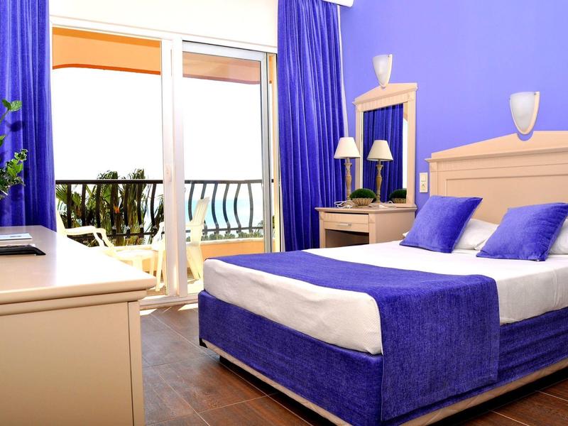 Helles Schlafzimmer mit blau-weißem Bett, Vorhängen, Balkon und Holzboden.