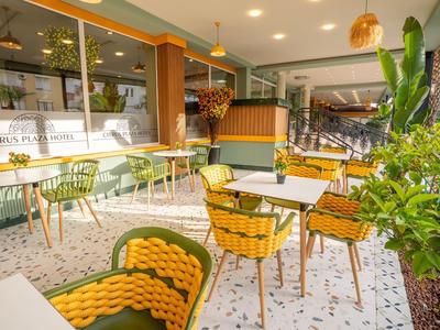 Helle Cafeteria mit grünen und gelben Stühlen, weißen Tischen, Pflanzen und hellen Lampen.