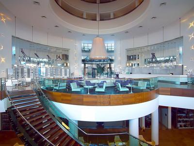 Großer, heller Salon mit runder Theke, modernen Treppen und vielen Bildschirmen, futuristisches Design.