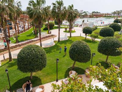 Grüner Park mit runden Büschen, Palmen und gepflasterten Wegen bei sonnigem Wetter.