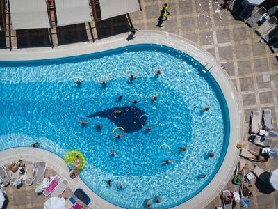 Überblick über einen runden Pool mit Menschen, blauen Fliesen und umliegenden Sonnenschirmen.