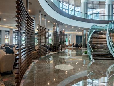 Moderne Lobby mit geschwungener Glas-Treppe, glänzendem Marmorboden und Holzverkleidungen.