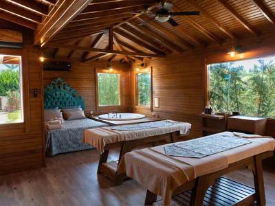 Gemütlicher Massageraum aus Holz mit zwei Liegen und großen Fenstern, viel natürlichem Licht.