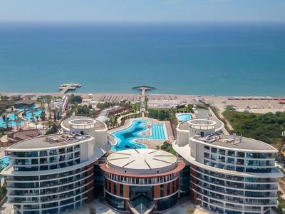 Luxushotel mit Rundbau, Poollandschaft und Strand am blauen Meer unter klarem Himmel.