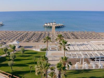 Strand mit Reihen von Sonnenschirmen, Palmen und einem Steg ins blaue Meer an einem sonnigen Tag.