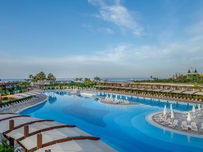 Großer Außenpool mit Liegestühlen und Sonnenschirmen in einem Hotelresort unter blauem Himmel.