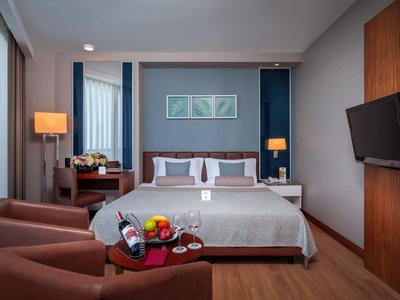 Modern eingerichtetes Hotelzimmer mit Doppelbett, Sitzbereich und Wandfernseher.