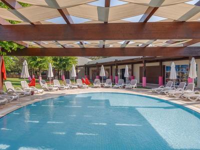 Poolbereich mit Liegestühlen unter einem Holzpergola und Sonnenschirmen in einem Hotel