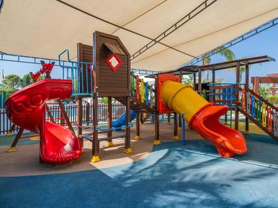 Bunter überdachter Spielplatz mit Rutschen und Klettergeräten auf weichem Bodenbelag.