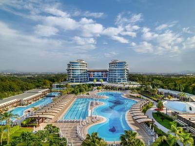 Großes Resort mit mehreren Schwimmbecken und Liegestühlen vor modernen Hotelgebäuden unter blauem Himmel.