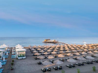 Strand mit Reihen von Sonnenschirmen und Liegen, blauer Himmel und steiniger Pier im Hintergrund