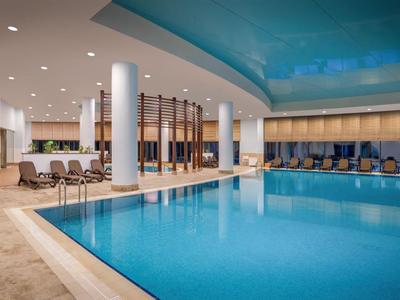 Großes, modernes Hallenbad mit blauen Wasser und Liegestühlen an den Seiten.