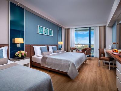 Modernes Hotelzimmer mit zwei Betten, Schreibtisch und Meerblick durch große Fenster.