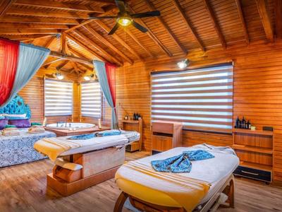 Gemütlicher Massageraum mit Holzwänden, zwei Behandlungsliegen und bunten Vorhängen.