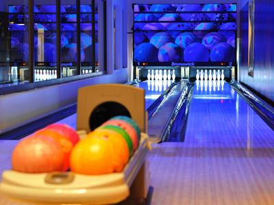 Blick auf eine leere Bowlingbahn mit bunten Bowlingkugeln im Vordergrund.