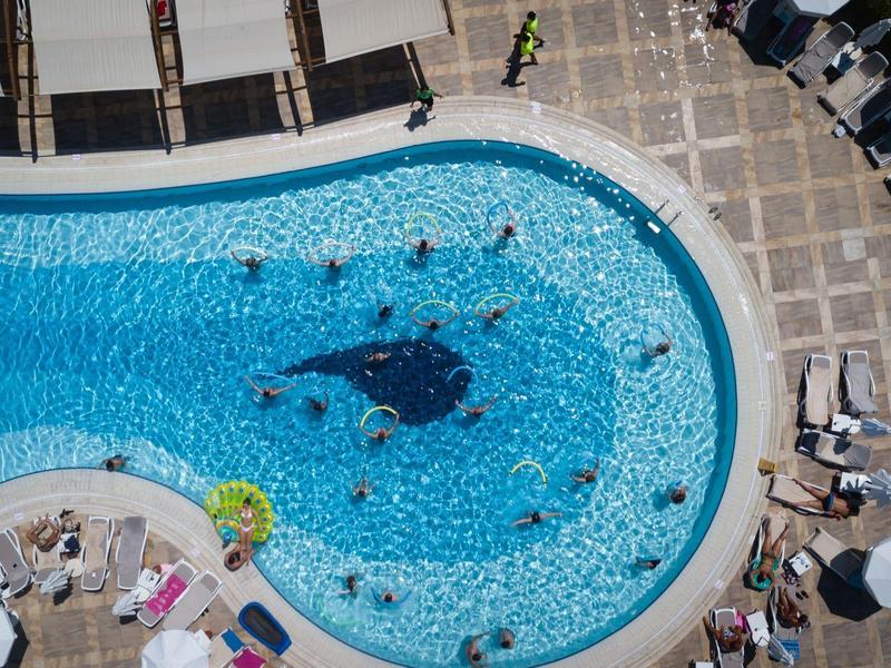 Überblick über einen runden Pool mit Menschen, blauen Fliesen und umliegenden Sonnenschirmen.