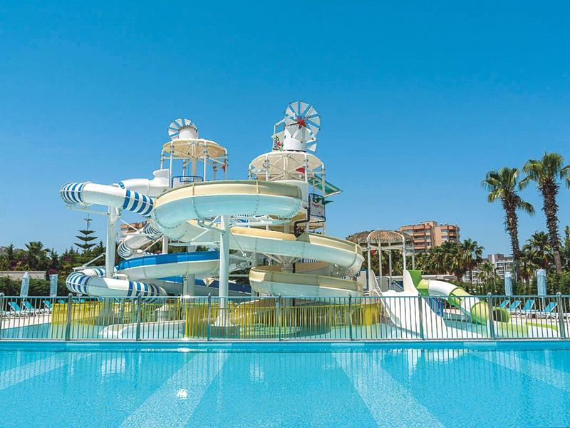 Riesige blaue und weiße Wasserrutsche mit Pool, umgeben von Palmen und blauem Himmel.