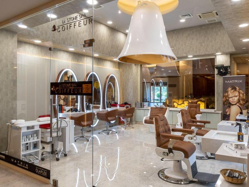 Moderner Friseursalon mit glänzendem Boden, Ledersesseln und großen Spiegeln an der Wand.