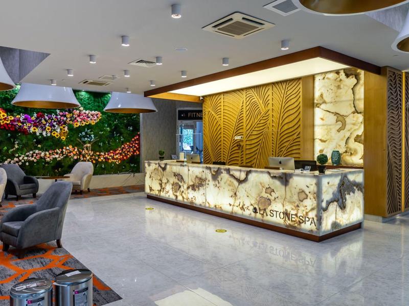 Modern gestalteter Empfang mit beleuchtetem Marmor-Tresen, grüner Pflanzwand und bequemen Sesseln.