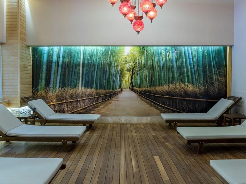 Ruheraum mit Holzliegen und großem Wandbild eines Bambuswegs, warmes Licht und Holzboden.