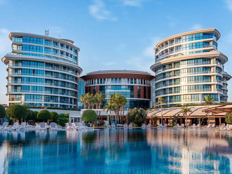 Modernes Hotel mit zwei runden Gebäuden, großem Pool und Palmen unter blauem Himmel.