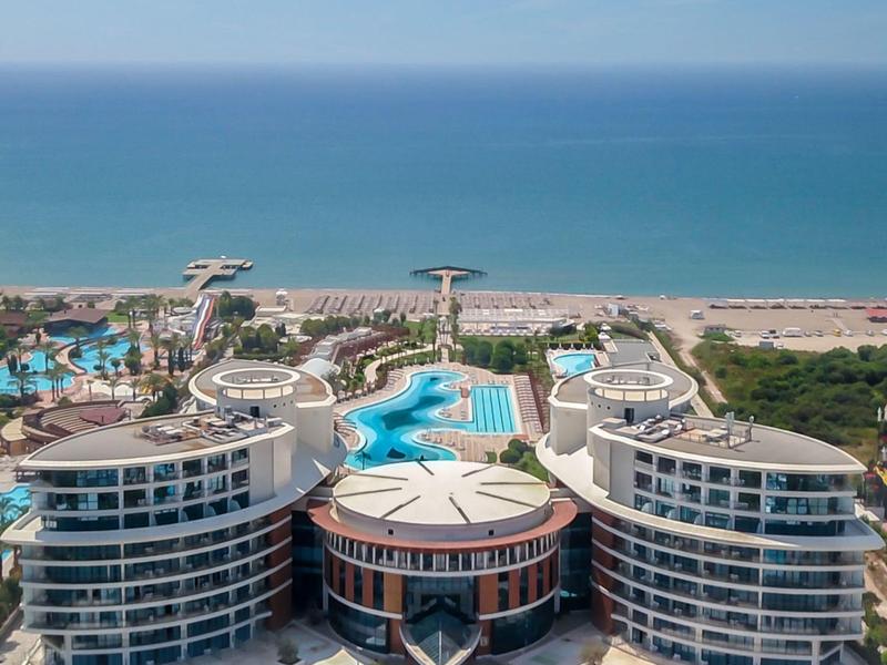 Luxushotel mit Rundbau, Poollandschaft und Strand am blauen Meer unter klarem Himmel.