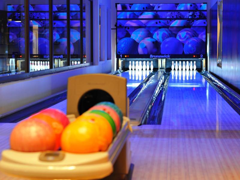 Bunte Bowlingkugeln liegen in der Bahn, hinten sind zehn klare Pins sichtbar.