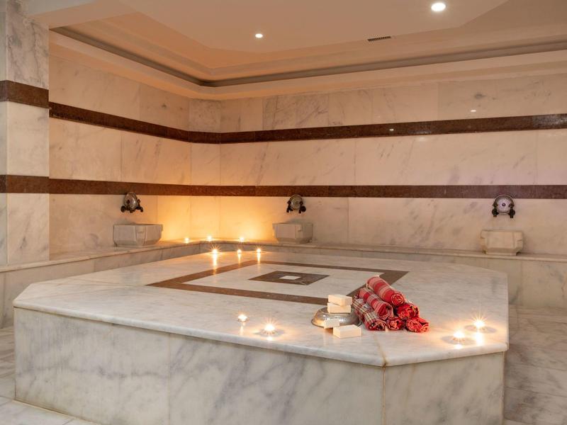 Großer Marmorraum mit zentraler Liege, warmem Licht und roten Rosen im Hammam.