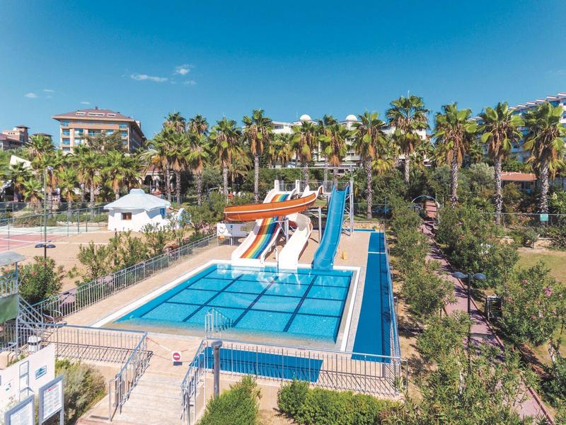 Wasserpark mit Rutschen, blauem Pool, Palmen und klar blauem Himmel im sonnigen Umfeld.