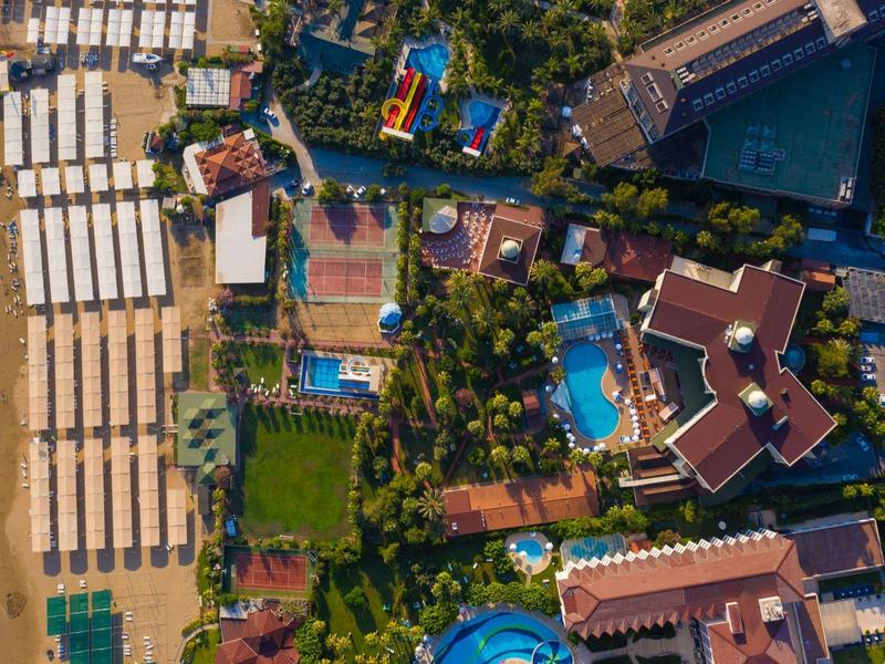 Luftaufnahme eines Resorts mit Swimmingpools, Liegestühlen am Strand und grünen Gartenanlagen.