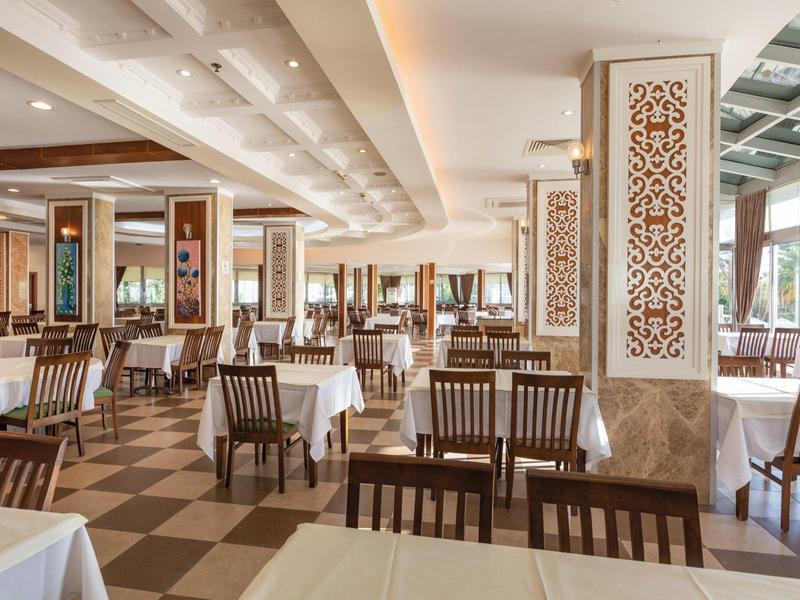 Großer, heller Speisesaal mit kariertem Boden, weißen Tischdecken und Holzmöbeln.