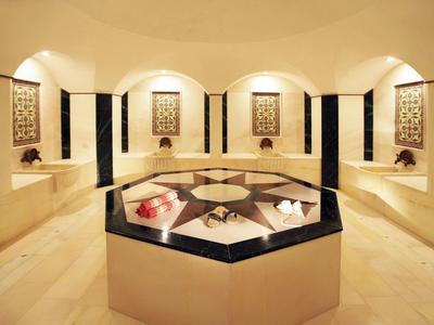 Un hammam di lusso con pareti in marmo e pannelli decorativi, isola centrale relax con asciugamani.