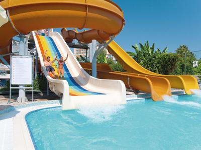 Parco acquatico con scivoli colorati che terminano in una piscina, giornata di sole.