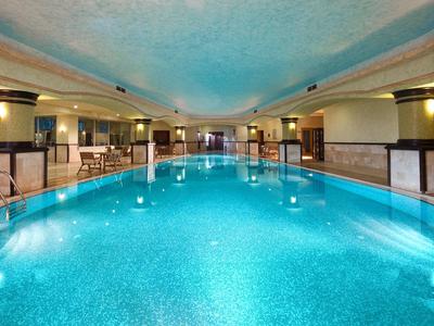 Grande piscina coperta con acqua blu e soffitto arrotondato illuminato.