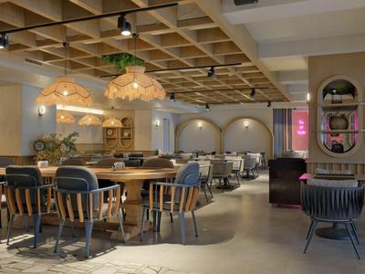 Modernes Restaurant mit Holztischen, runden Stühlen und dekorativen Hängelampen in warmem Licht.