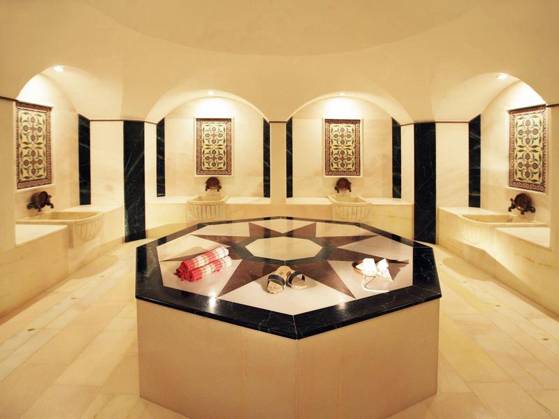 Un hammam di lusso con pareti in marmo e pannelli decorativi, isola centrale relax con asciugamani.