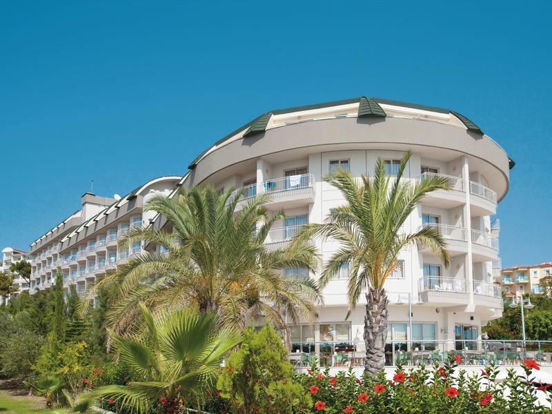 Edificio dell'hotel con balconi moderni, palme e fiori sullo sfondo con cielo limpido.