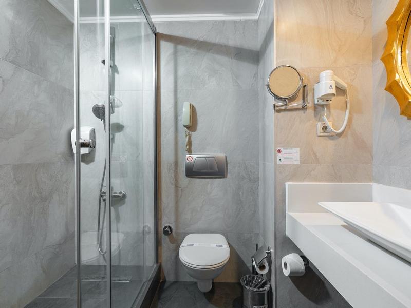 Bagno moderno con doccia, WC, lavabo e asciugacapelli a muro in toni neutri.