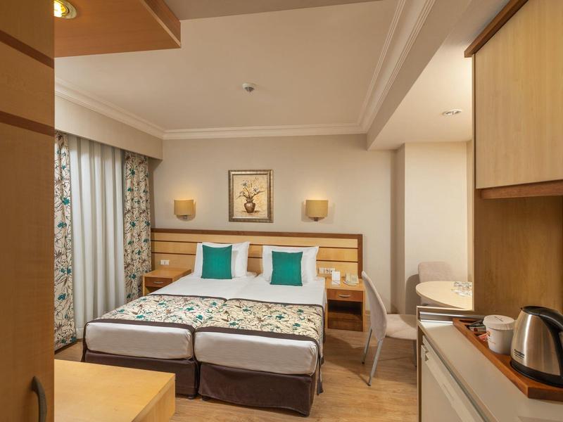 Camera d'hotel accogliente con letto matrimoniale, comodini e piccolo angolo cottura.