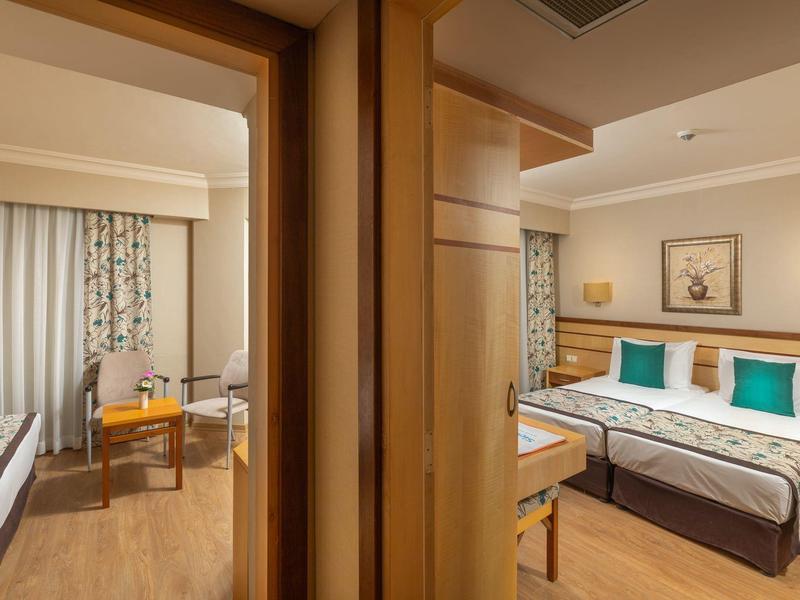 Due camere d'hotel adiacenti con letti, mobili in legno e luce calda.