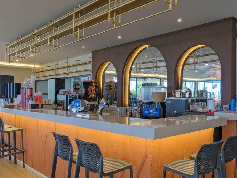 Bar moderna con bancone illuminato, sgabelli neri e finestre rotonde.