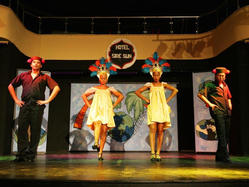 Due uomini e due donne in costumi colorati sul palco davanti a un'insegna dell'hotel.