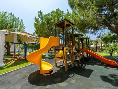 Kinderspielplatz mit Rutschen und Terrasse in einem grünen, sonnigen Hotelgarten.
