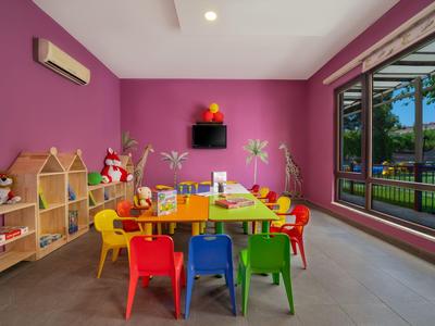 Bunter Kinderspielraum mit Tischen, Stühlen und großer Fensterfront in einem Hotel.